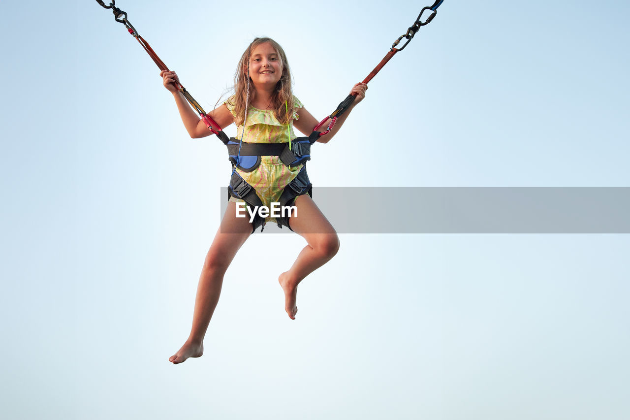 Bungee jumping at trampoline. little girl bouncing on bungee jumping in amusement park on summer day