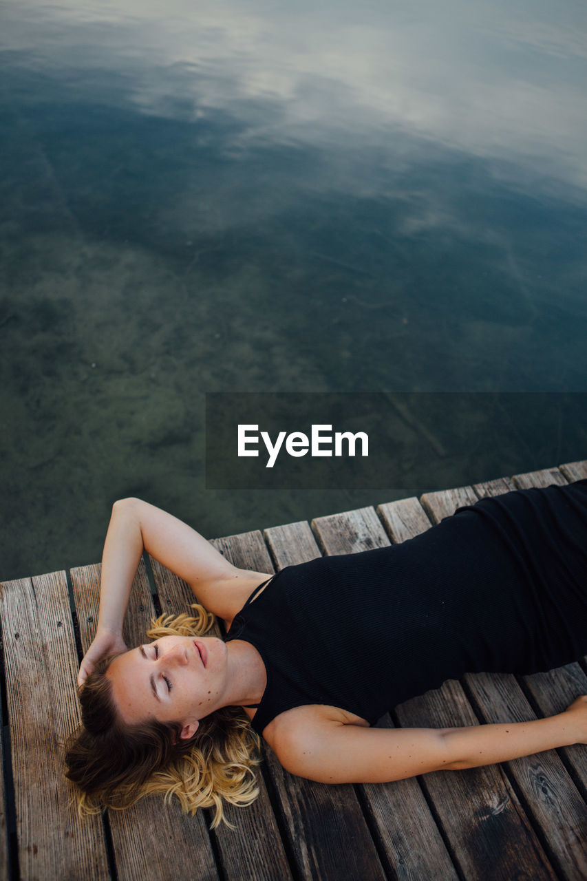 Woman lying down on pier by river against sky