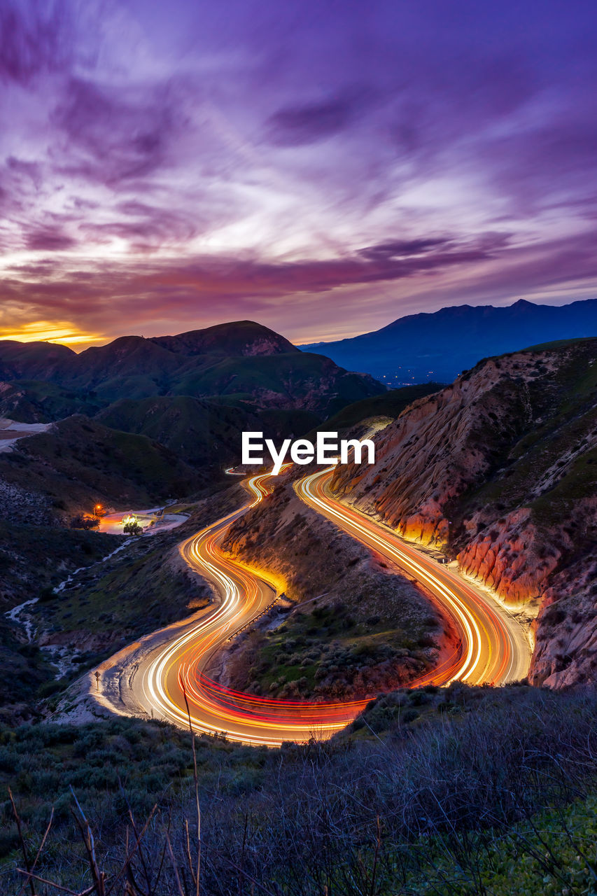 High angle view of light trails on winding mountain road against sky at sunset