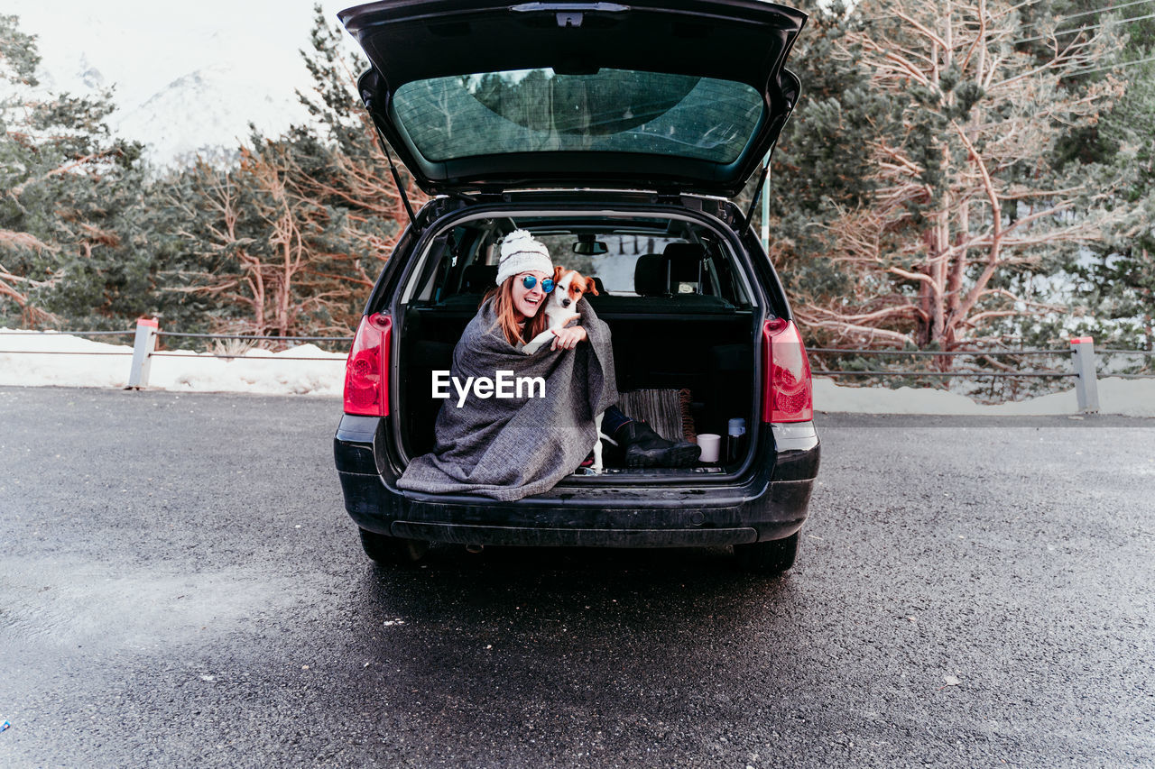 Woman holding dog while sitting in car trunk