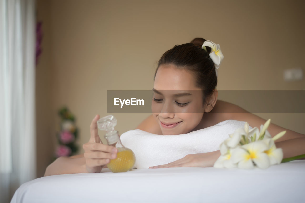 Smiling young woman with oil lying on massage table in spa