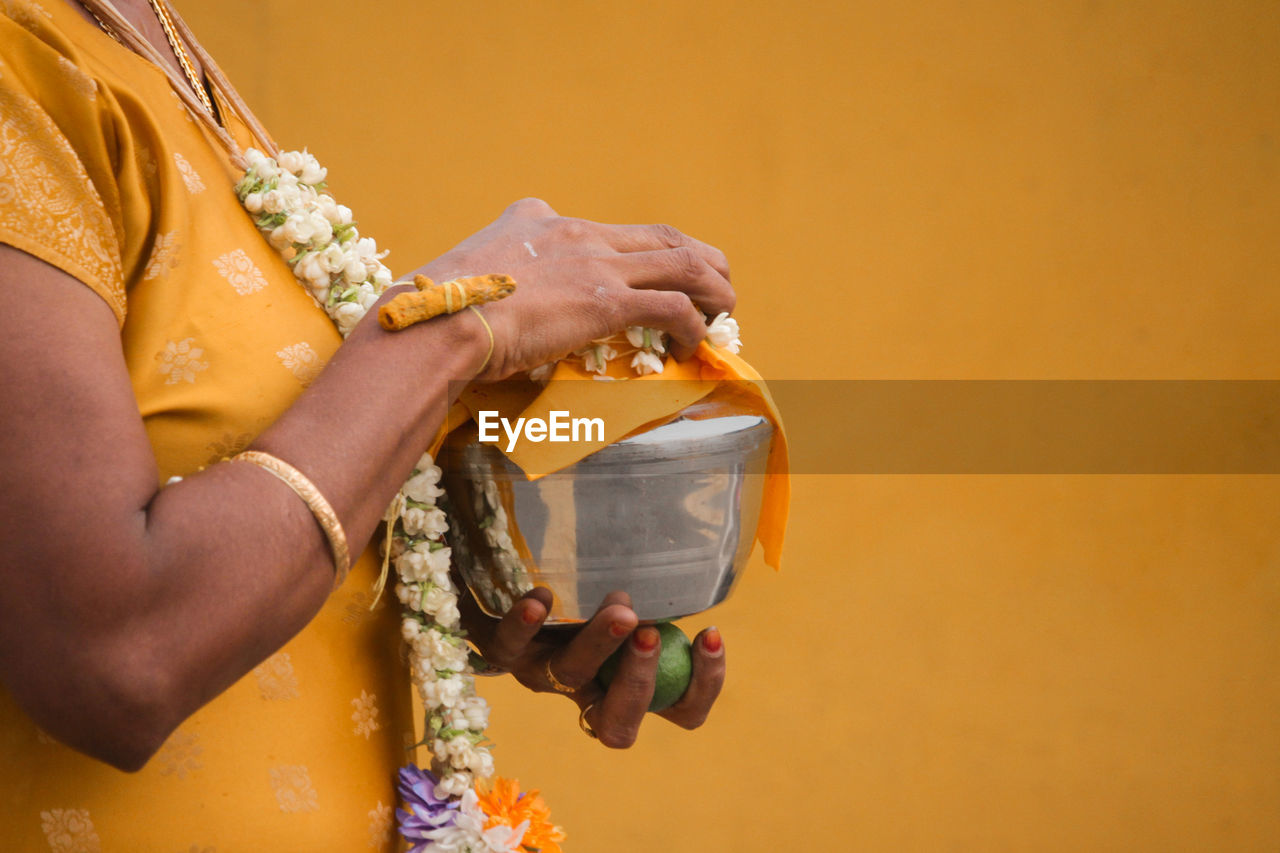 Midsection of woman holding religious utensil against yellow