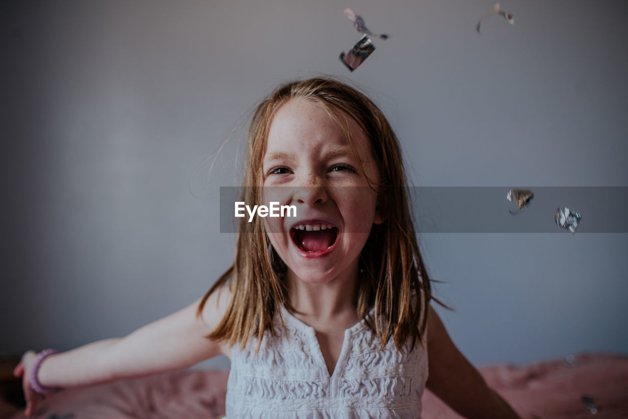 Portrait of young girl happily throwing silver confetti