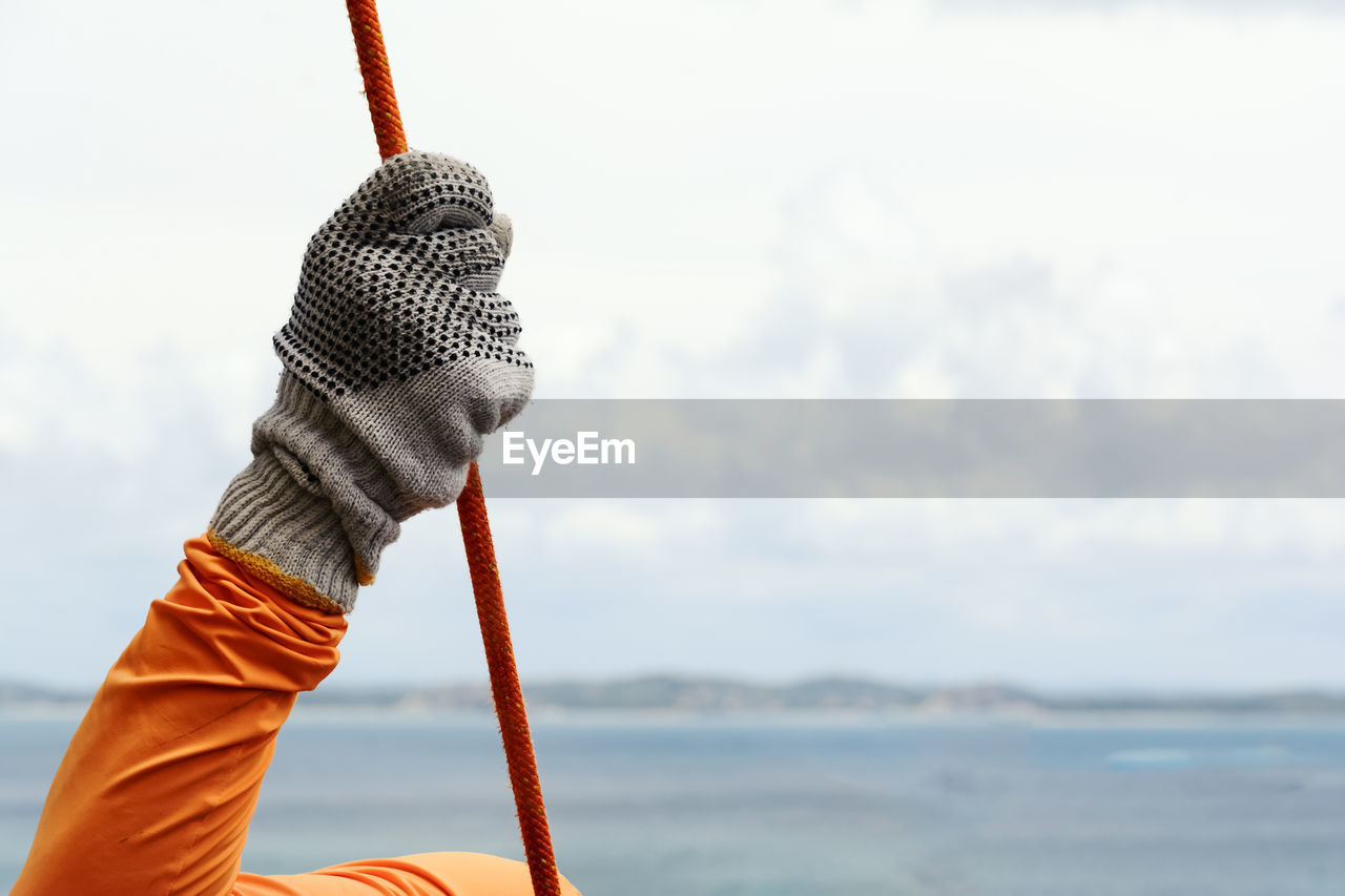 Close-up of hand with glove holding a rope against the sky.