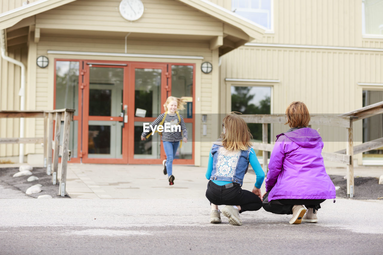 Girl running from school towards mother