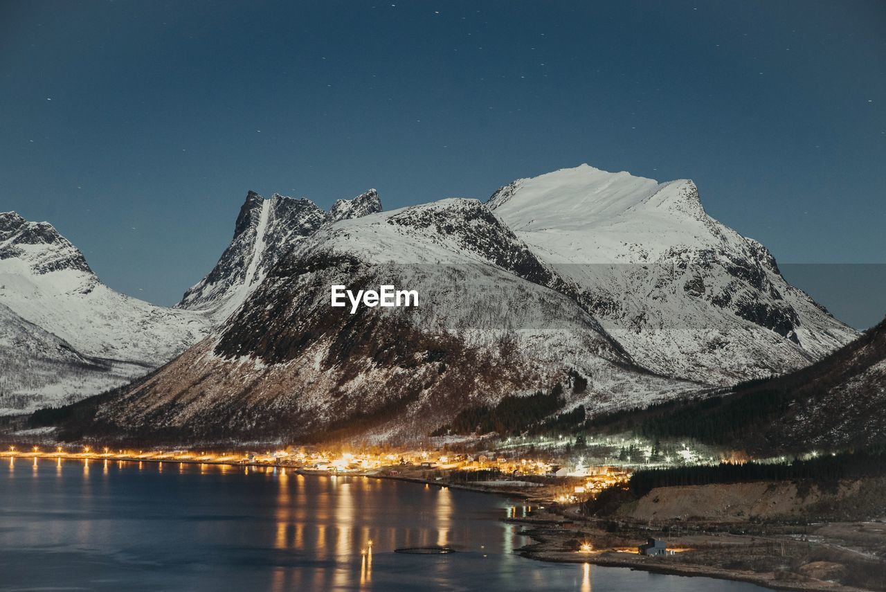 SCENIC VIEW OF LAKE BY SNOWCAPPED MOUNTAINS AGAINST SKY AT NIGHT DURING WINTER