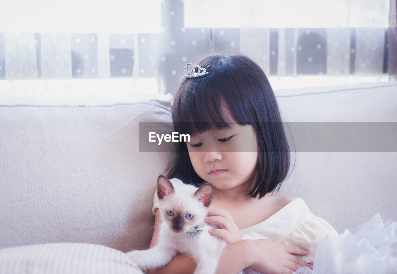 Cute girl with kitten sitting on sofa at home