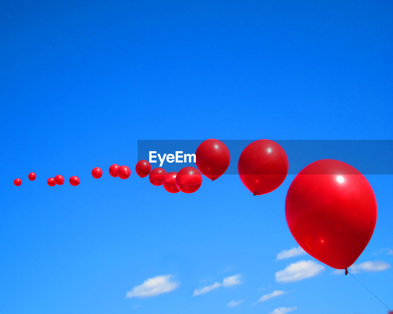 Low angle view of red balloons against blue sky on sunny day