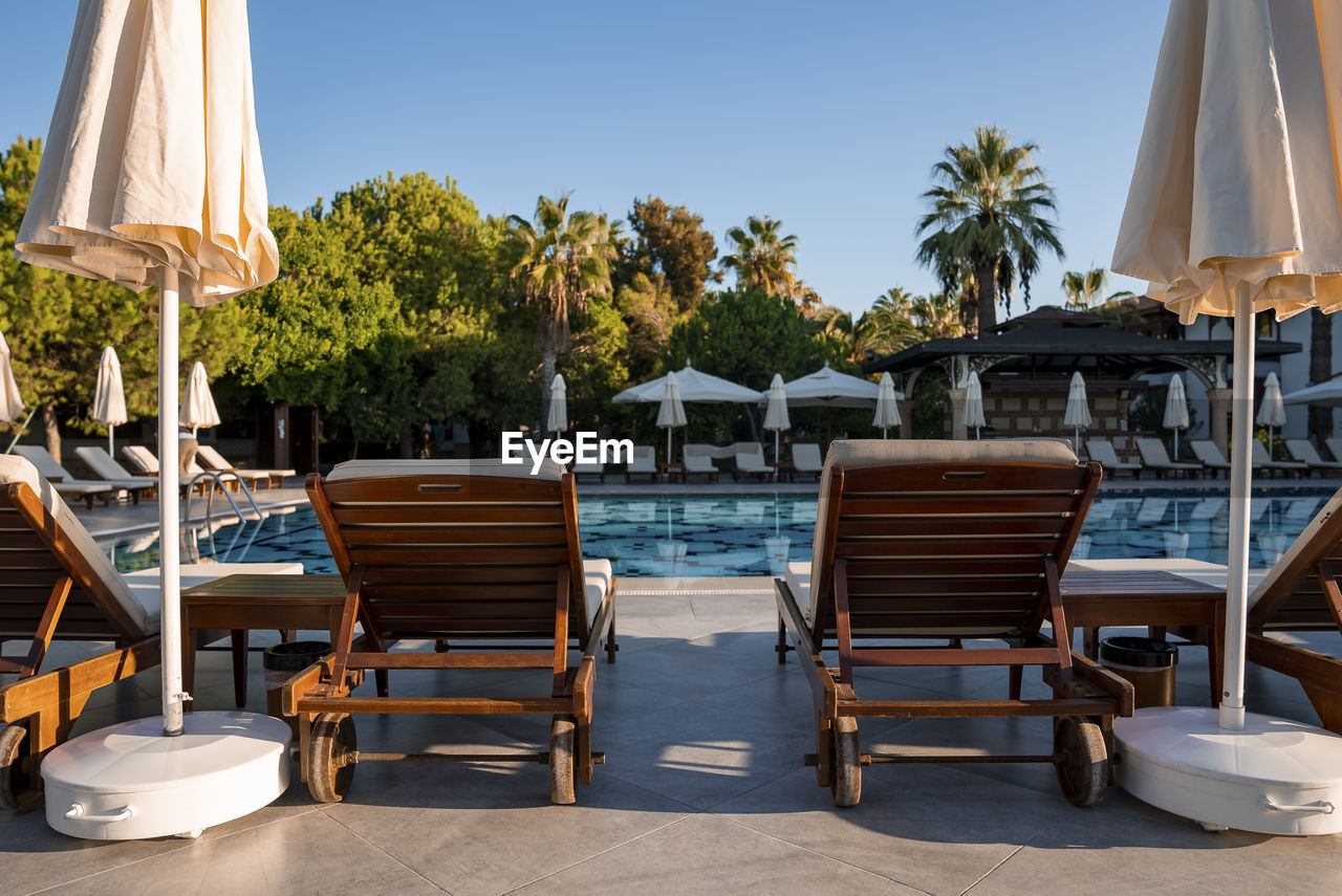 Empty deck chairs and white parasols arranged at poolside in tourist resort