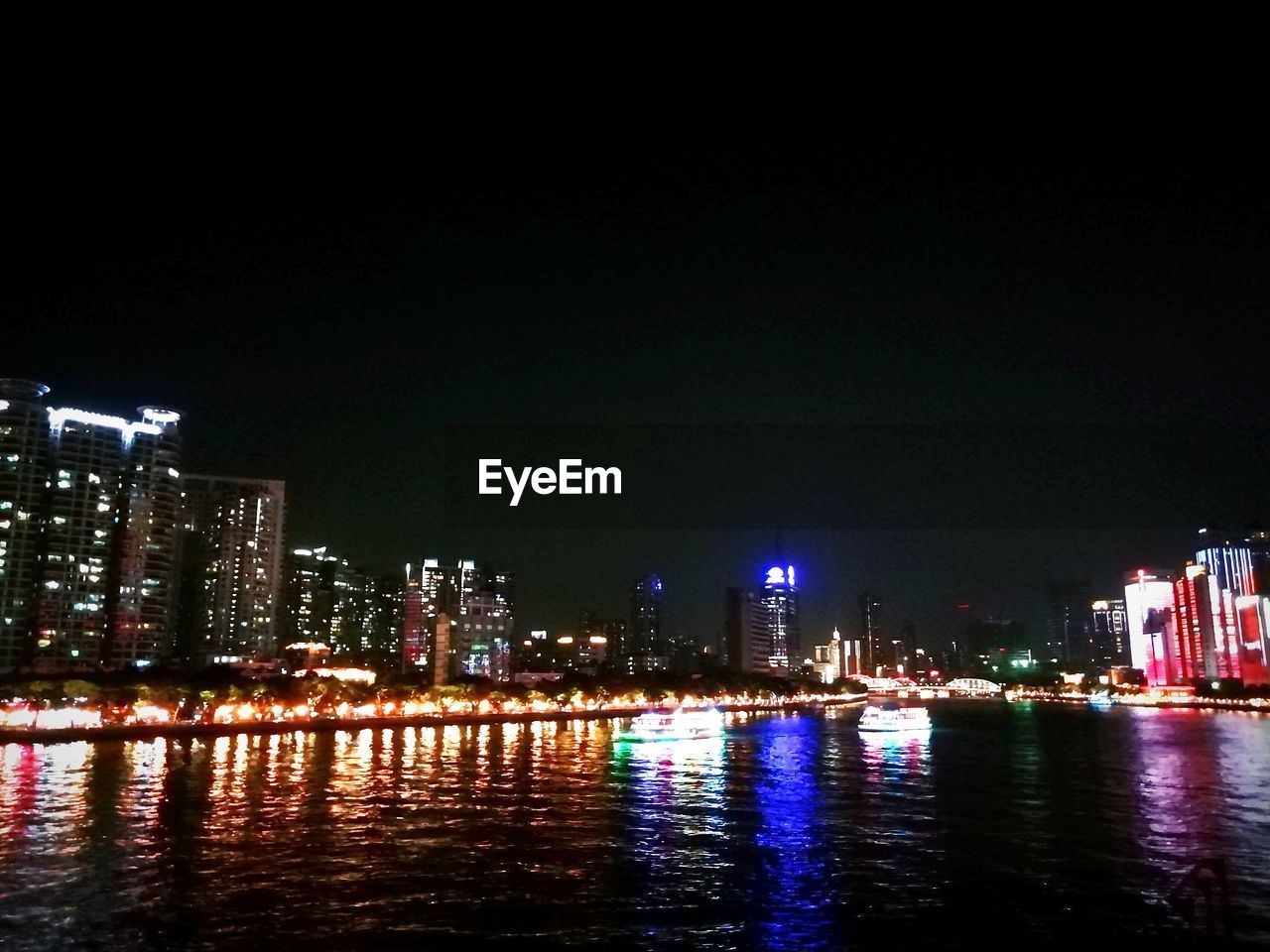 ILLUMINATED BUILDINGS BY RIVER AGAINST SKY