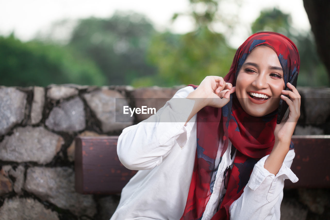 Cheerful young woman wearing hijab while talking on smart phone