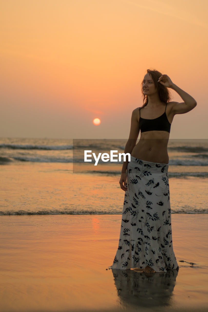 Full length of woman standing at beach against sky during sunset