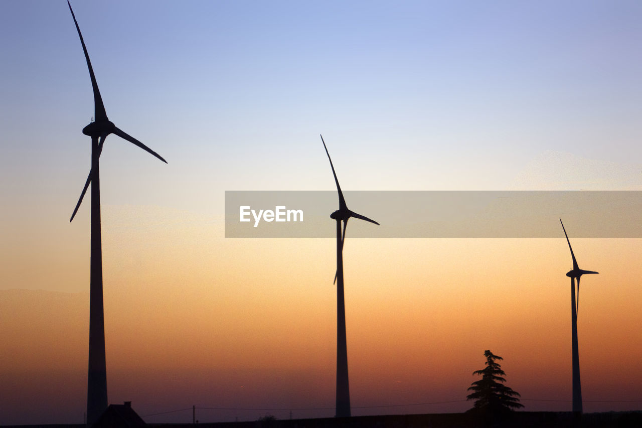 Silhouette wind turbines on field against sky during sunset