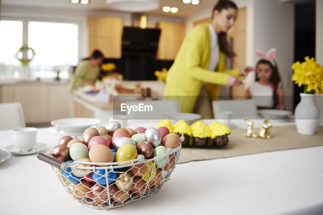 Easter eggs in basket on table at home with mother and daughter in background