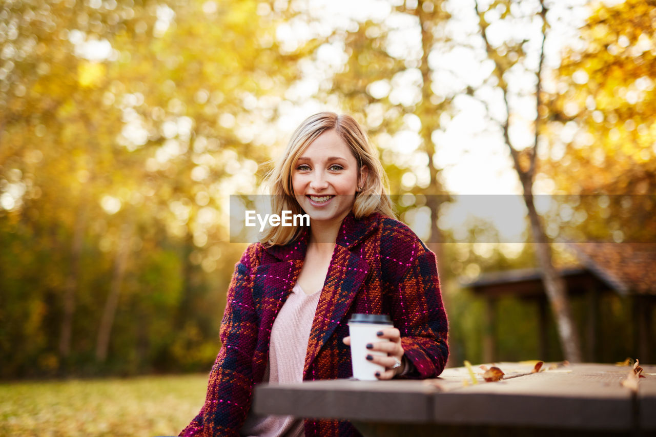 Young woman sitting on picnic table in park during autumn