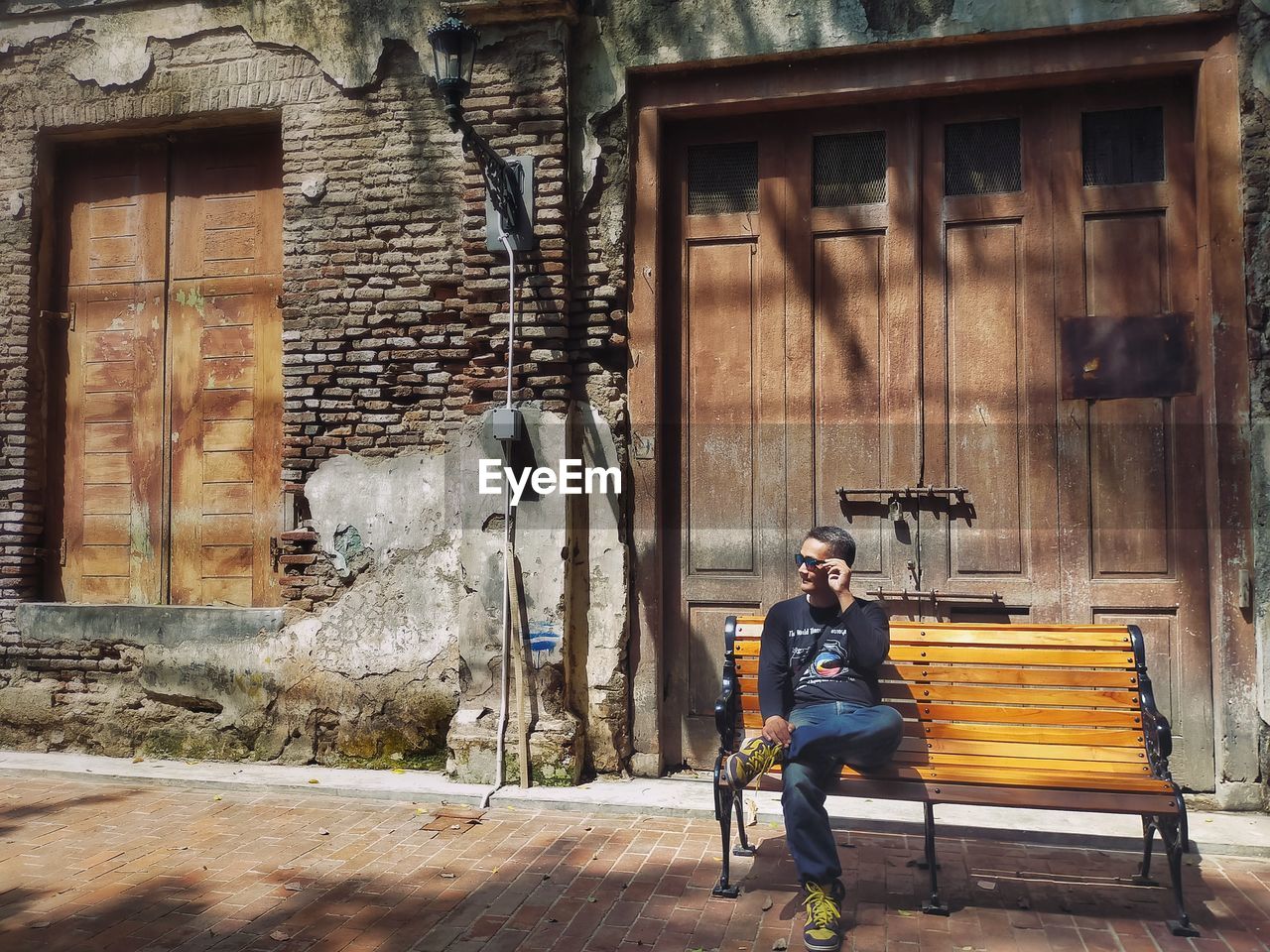 Full length of man sitting on bench against building