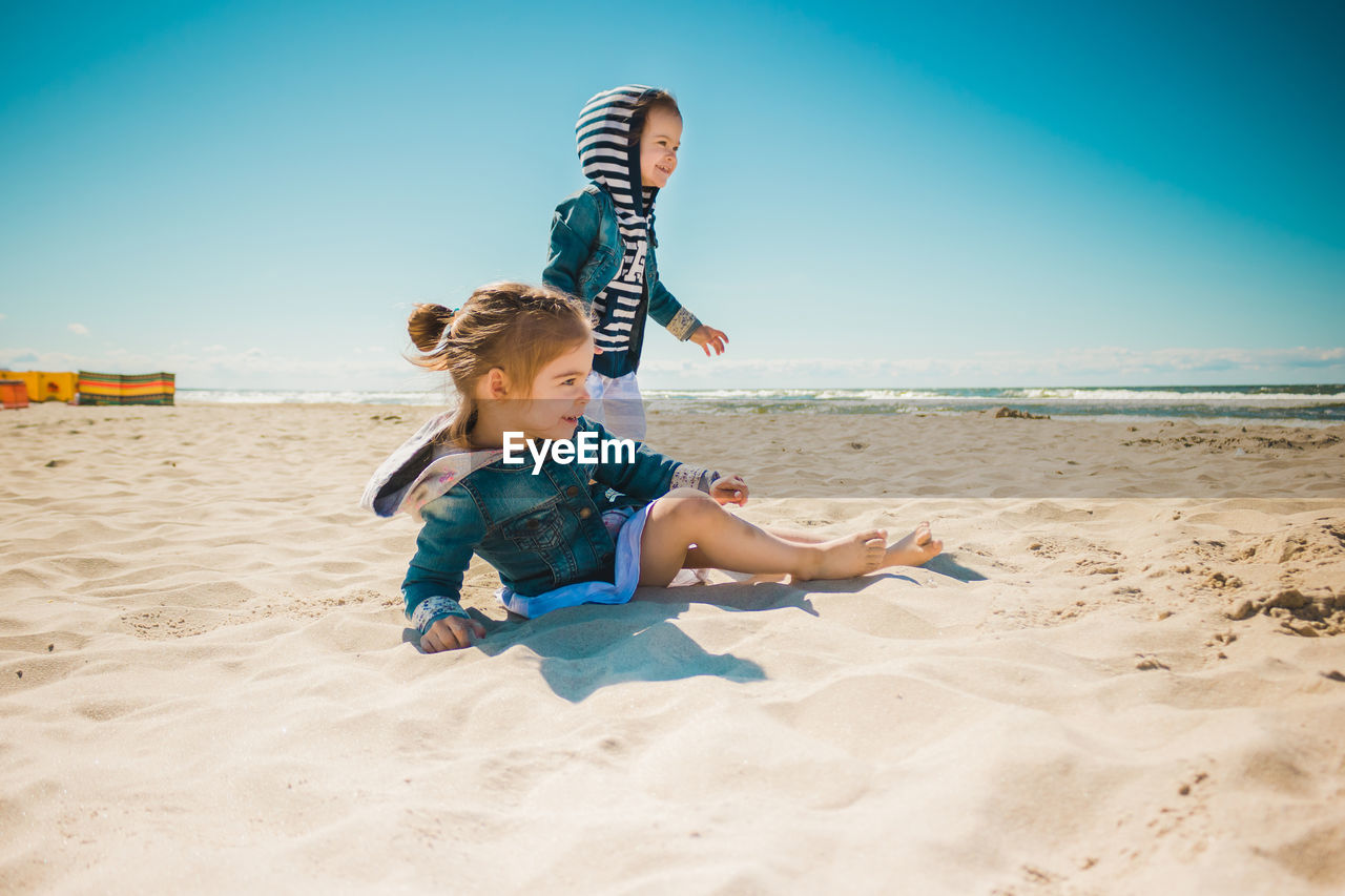 Siblings playing with sand at beach against sky