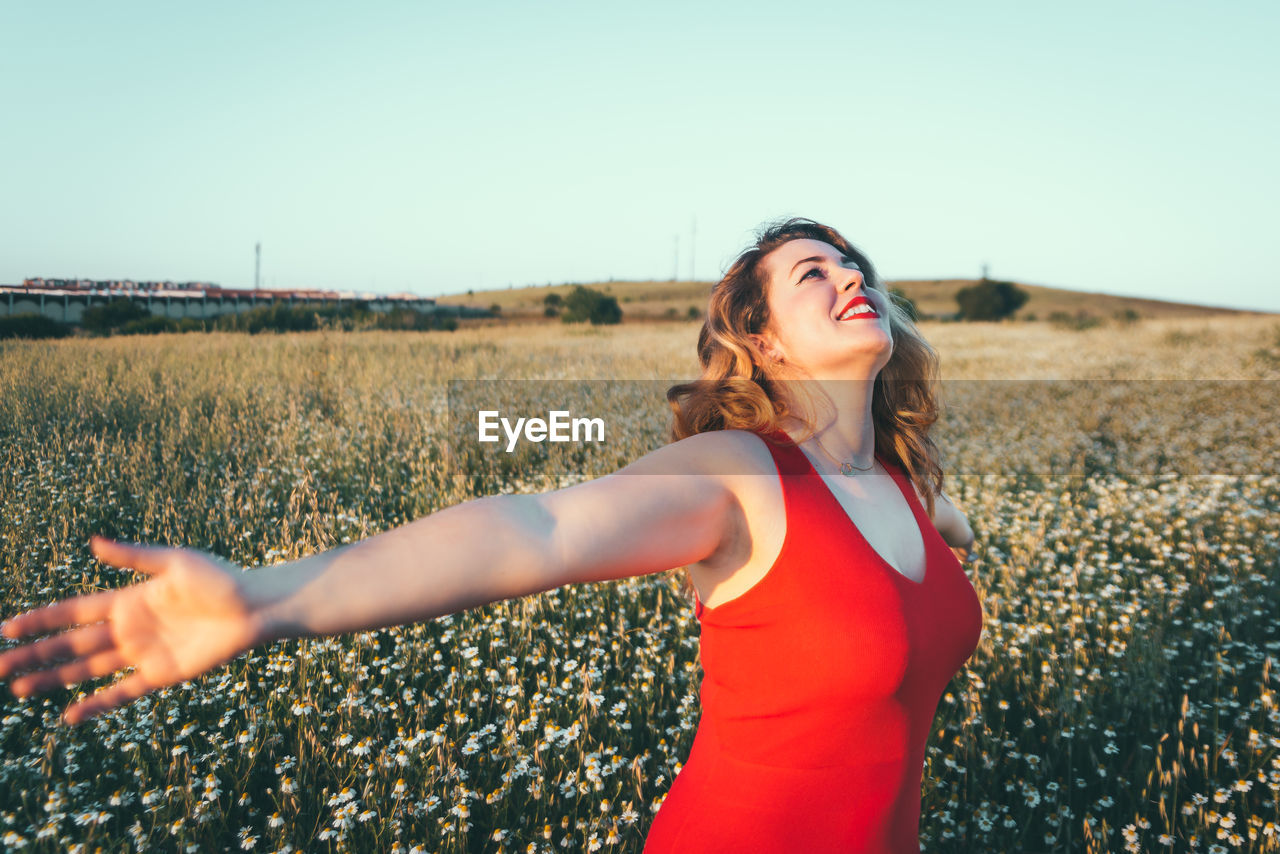 Beautiful young woman standing on field against clear sky