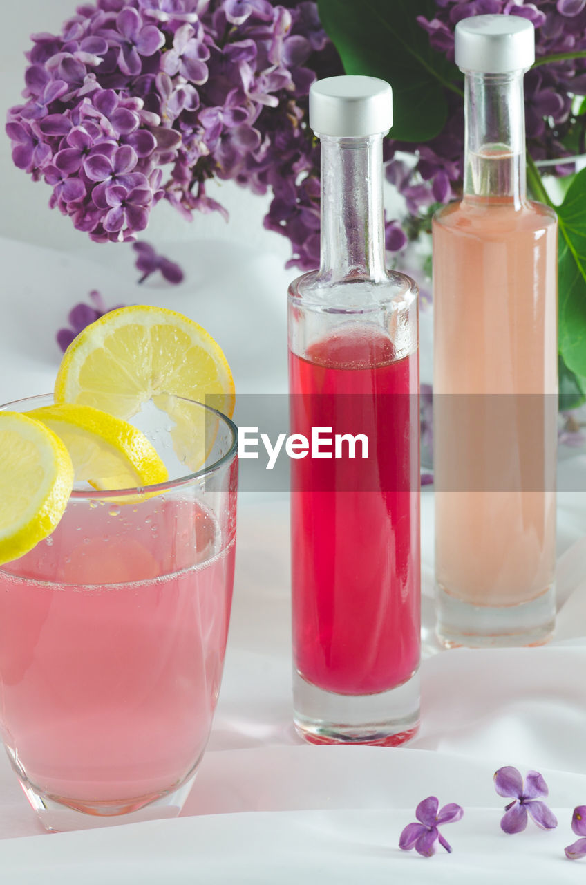 Colorful drinks by purple lilac flowers on table