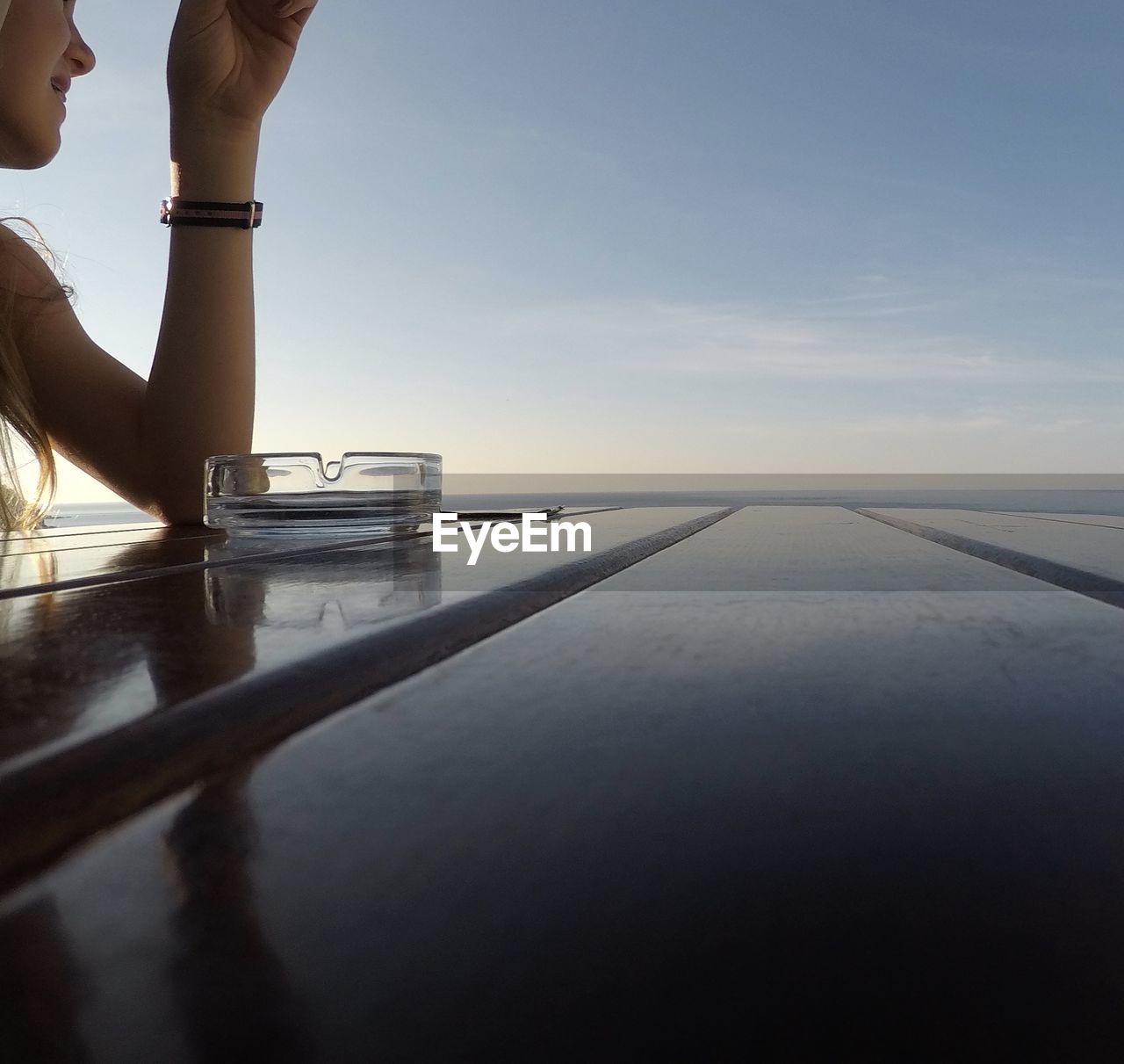 LOW SECTION OF WOMAN ON TABLE AGAINST SEA AT SUNSET