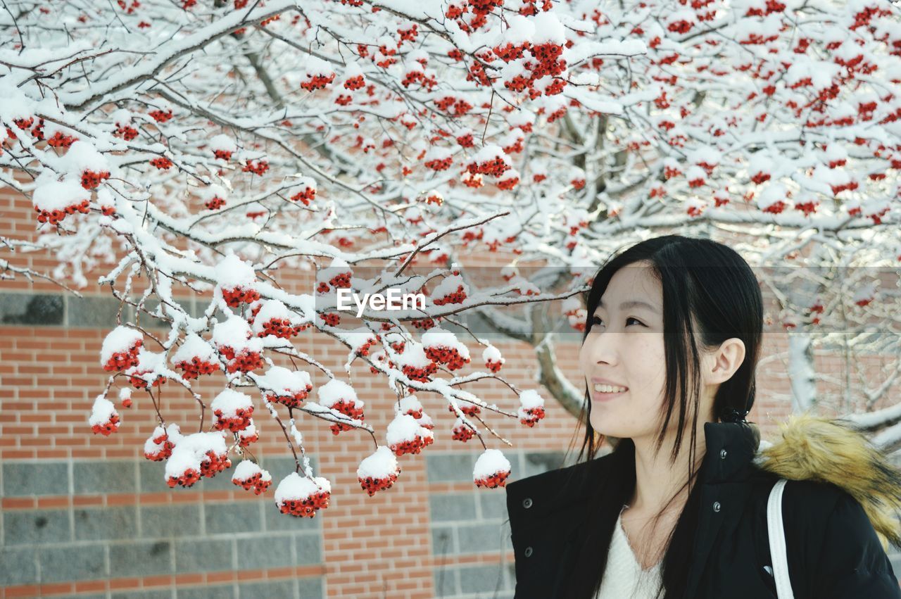 Smiling young woman looking at snow covered berries at yard