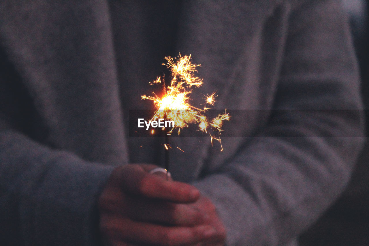 Midsection of person holding sparkler at night