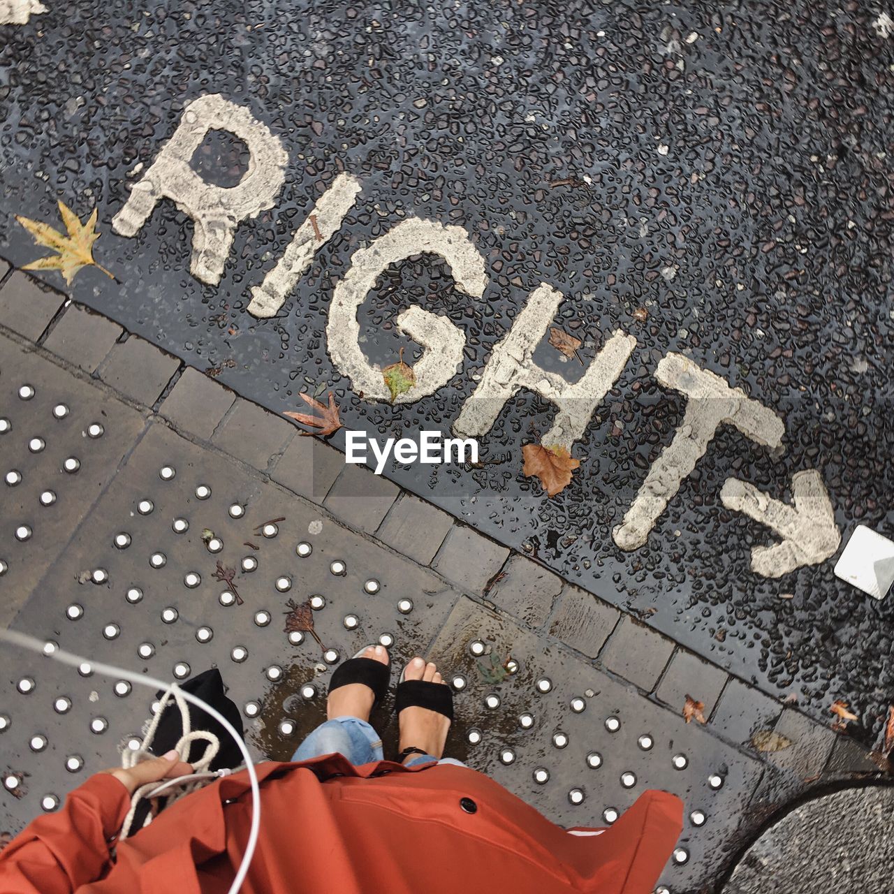 Low section of woman standing on wet footpath by text during monsoon