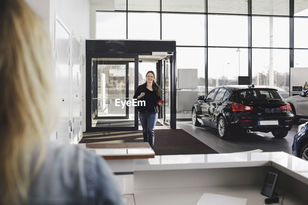 Smiling woman walking towards sales clerk at car showroom