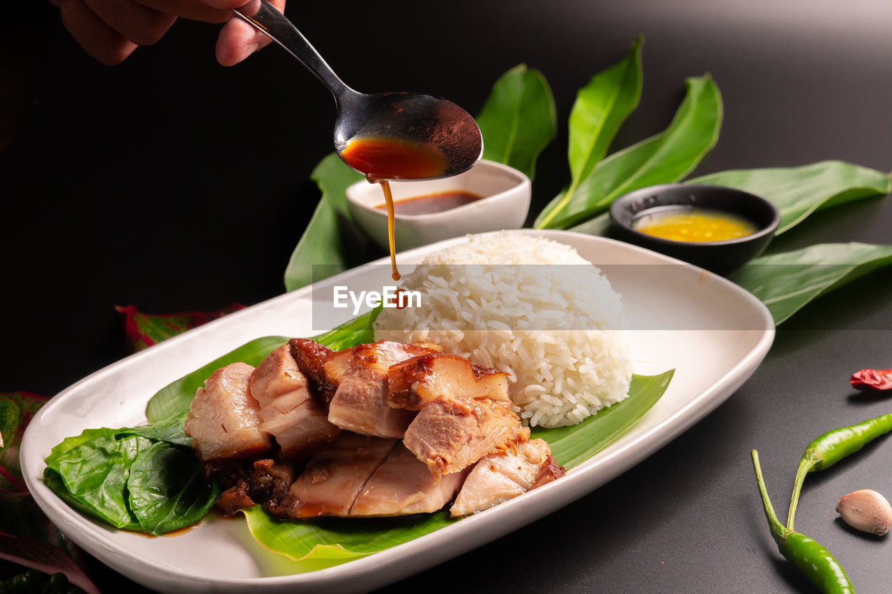 Cropped hand mixing sauce in meat on plate