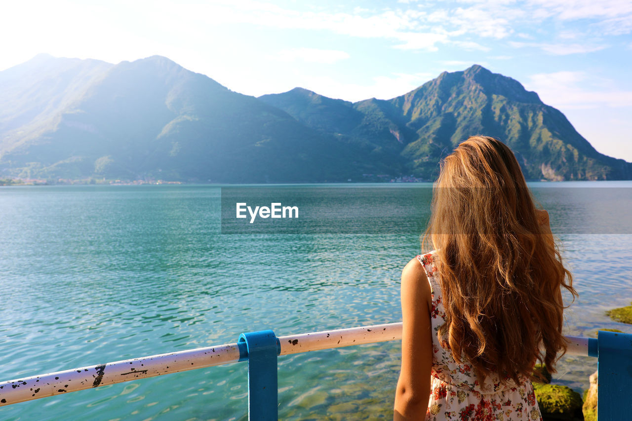 Rear view of woman looking at lake by mountains