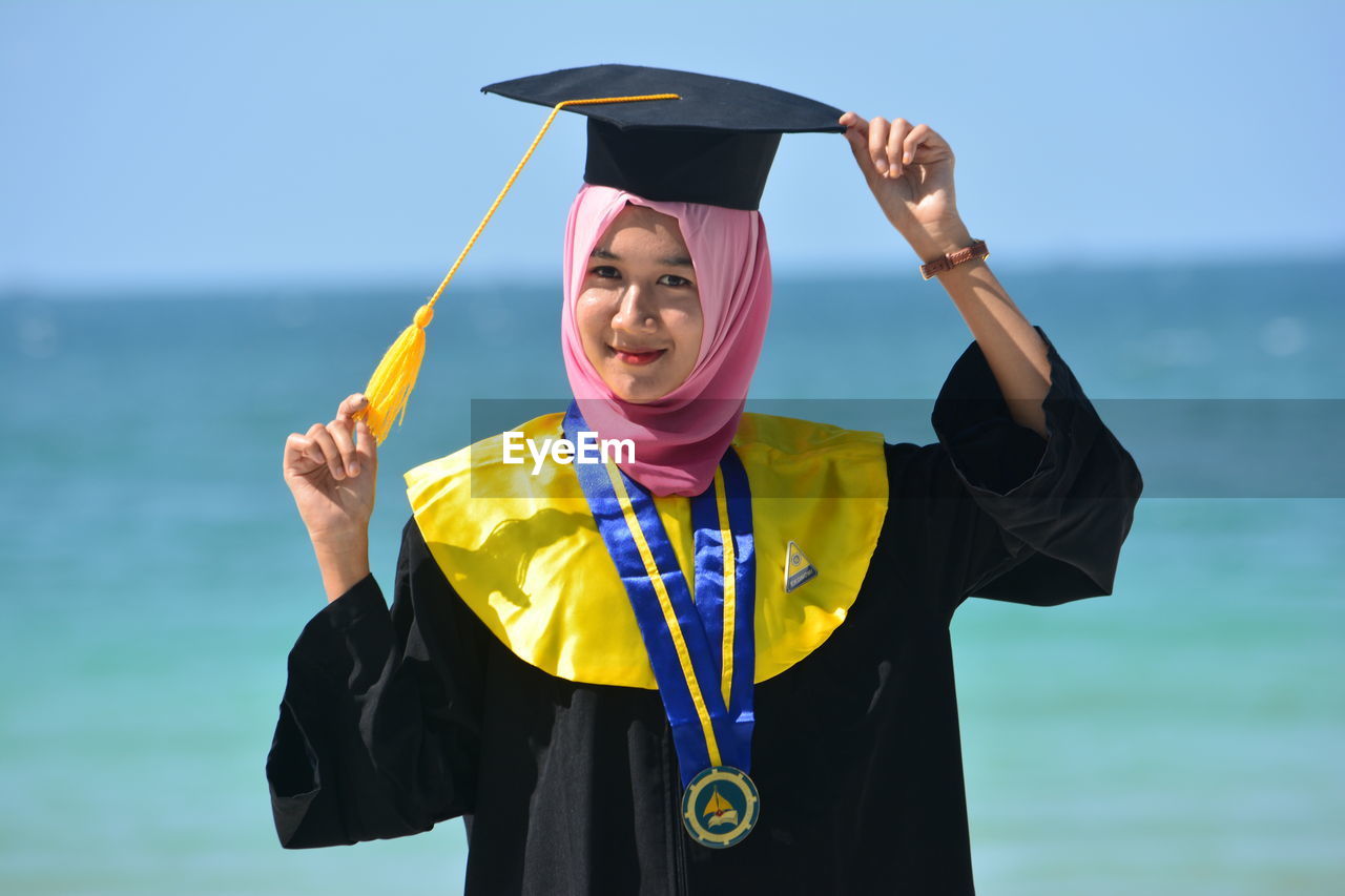 Portrait of woman in hijab wearing mortarboard while standing against sea