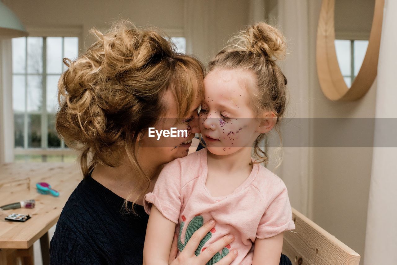 Mother and daughter hugging whilst playing with make up at home