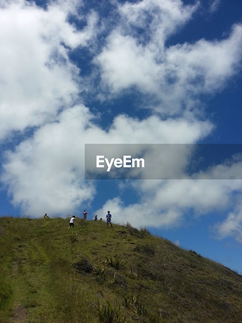 LOW ANGLE VIEW OF MAN WALKING ON MOUNTAIN AGAINST SKY