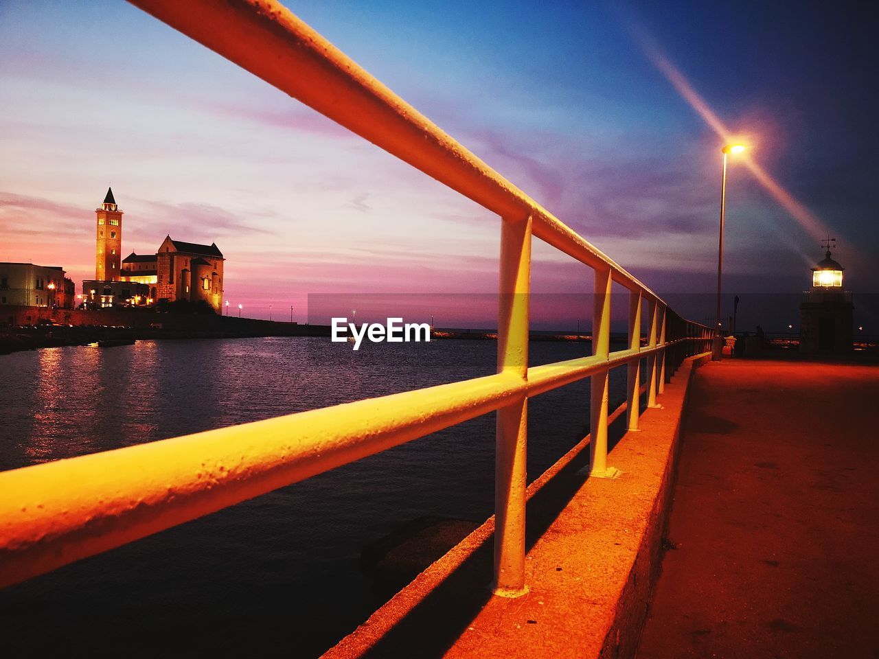 ILLUMINATED BRIDGE BY SEA AGAINST SKY AT SUNSET