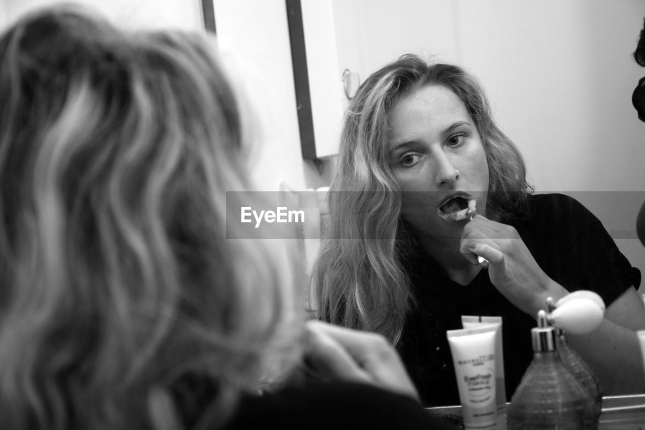 Young woman brushing teeth in front of mirror