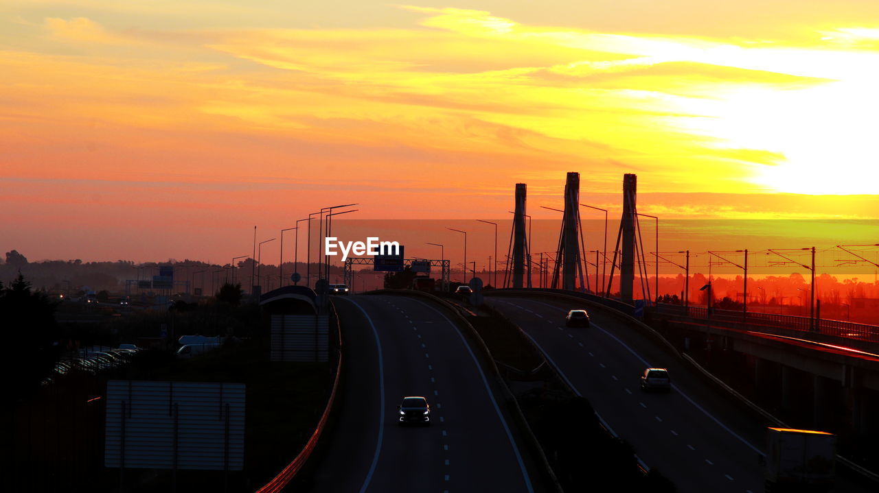 Cars moving on highway against sky during sunset