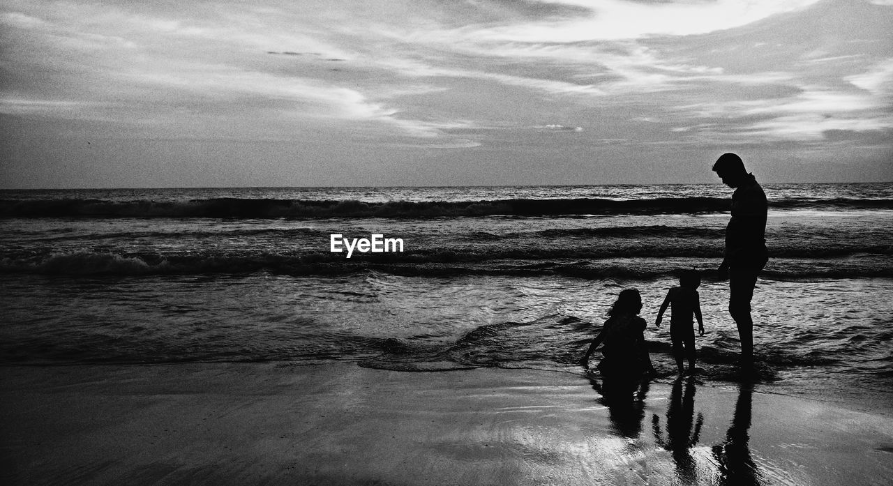 Silhouette family standing on beach against sky