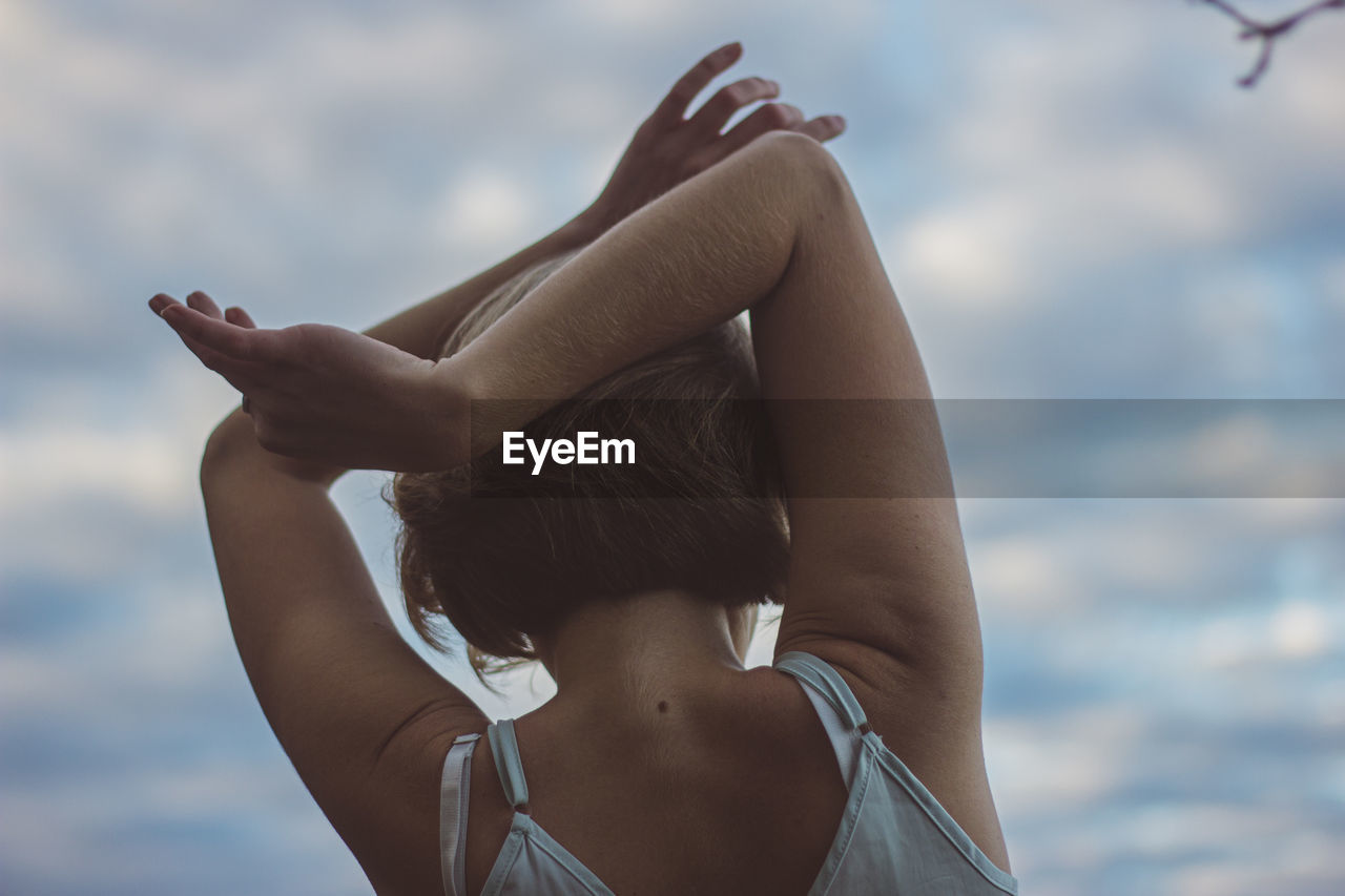 Rear view of woman with arms raised dancing against sky