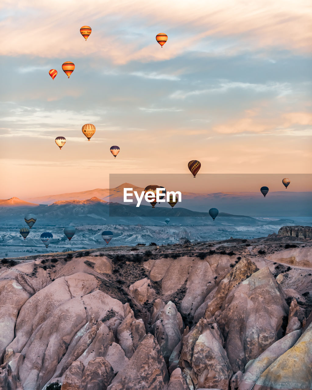 Hot air balloons flying over rocks against sky during sunset