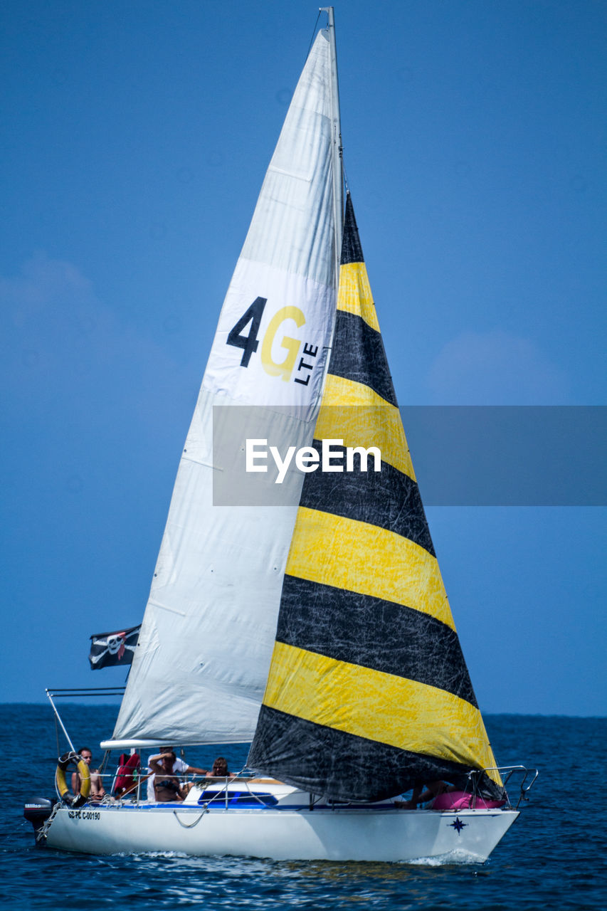 People enjoying in sailboat moving on sea against clear blue sky