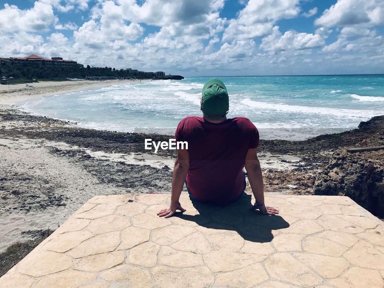 Rear view of man sitting at beach against sky