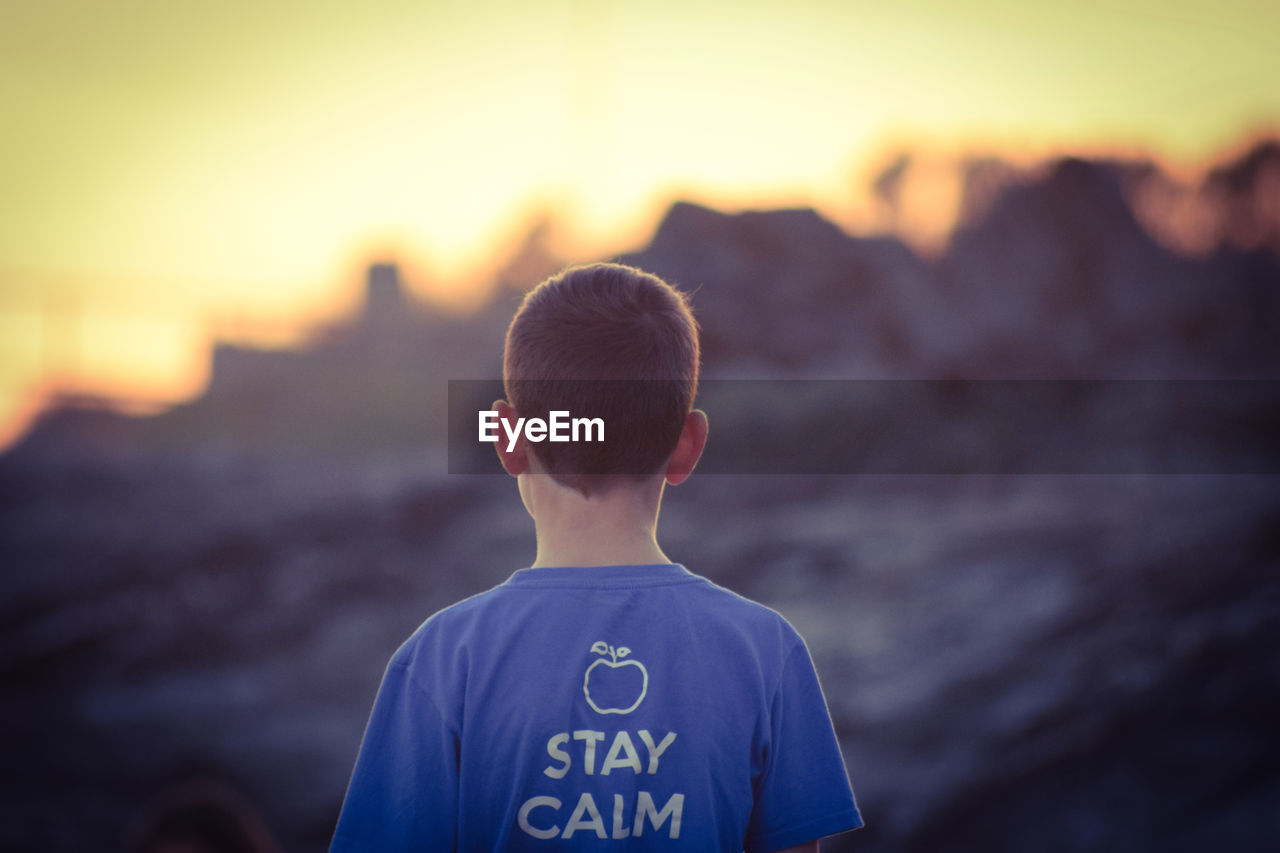 Rear view of boy standing against sky during sunset