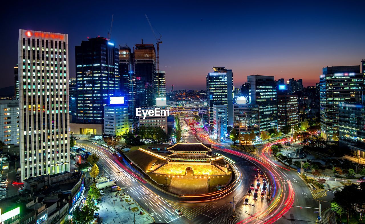 HIGH ANGLE VIEW OF ILLUMINATED STREET AMIDST BUILDINGS IN CITY