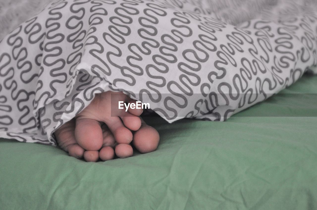 Low section of person covered with blanket on bed