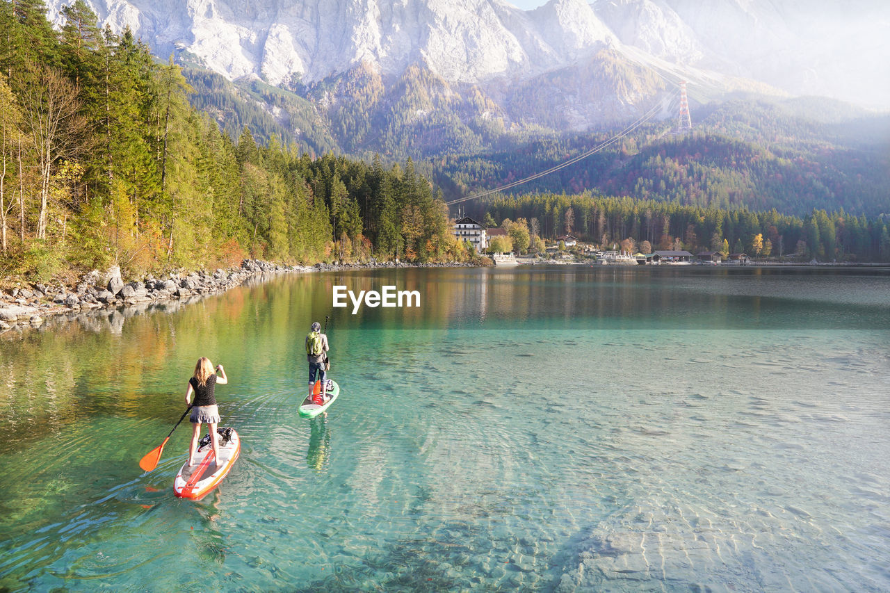 Man and woman rowing boat in lake against mountains