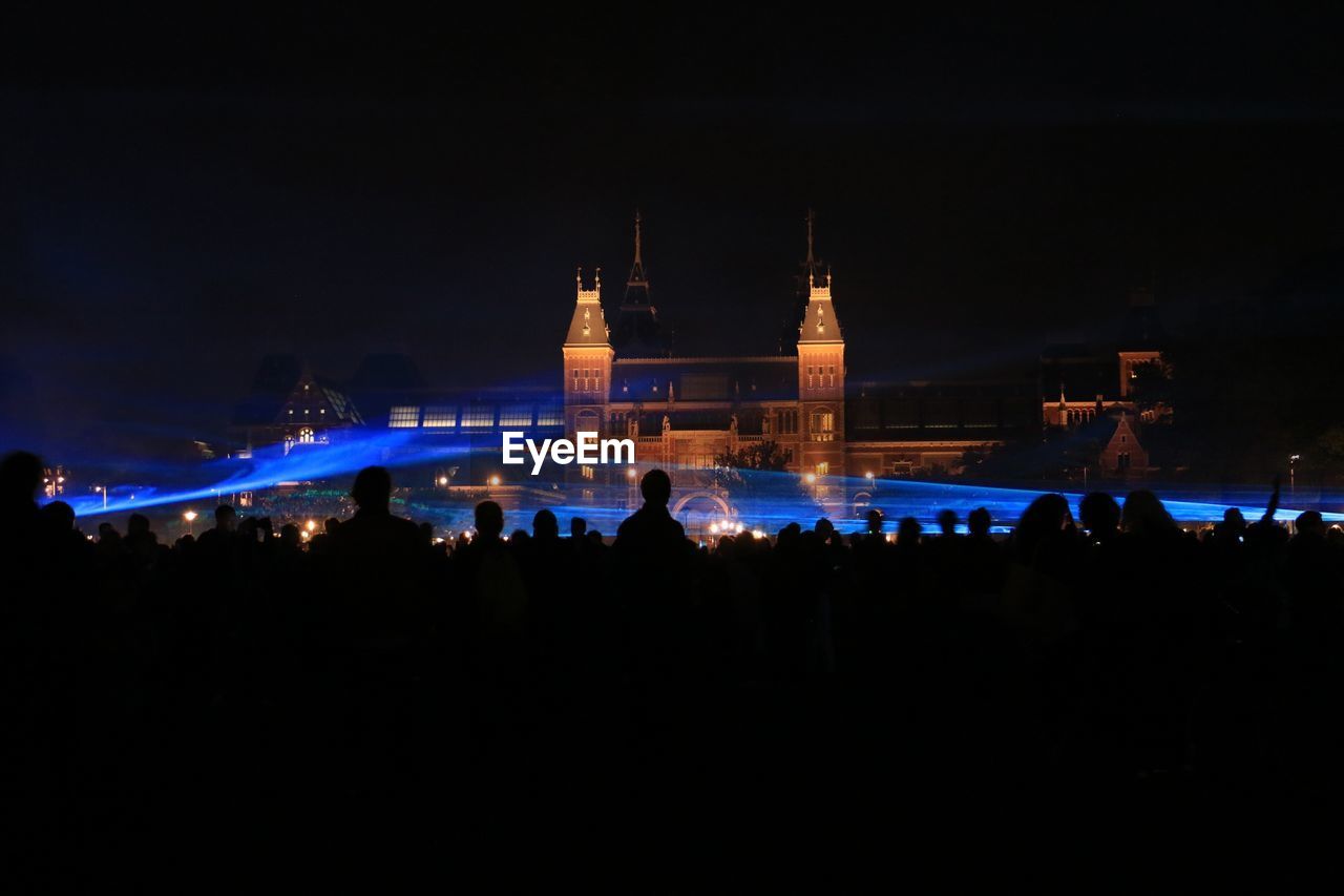 People by illuminated waterlicht against rijksmuseum at night