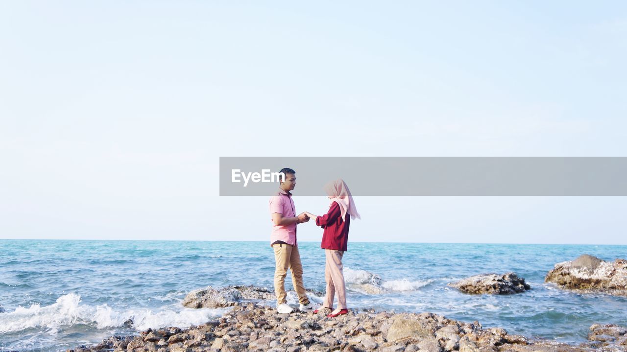 Couple standing on rock against clear sky