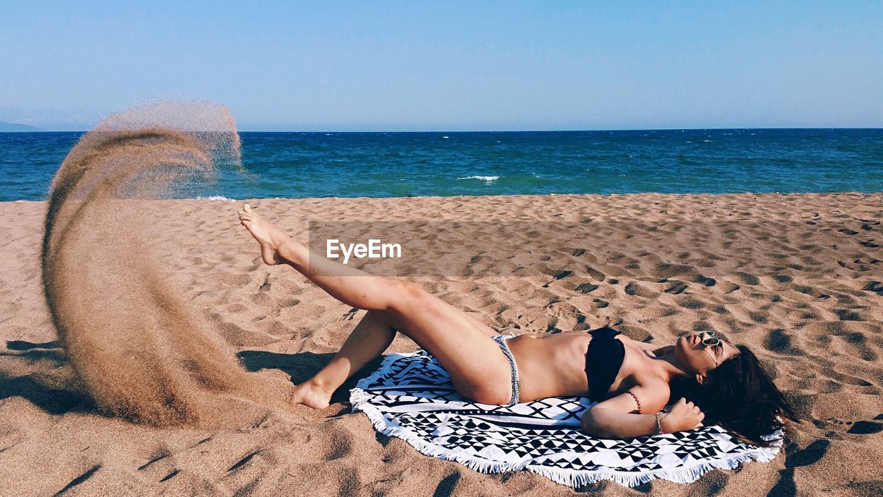 Woman lying on beach against clear sky