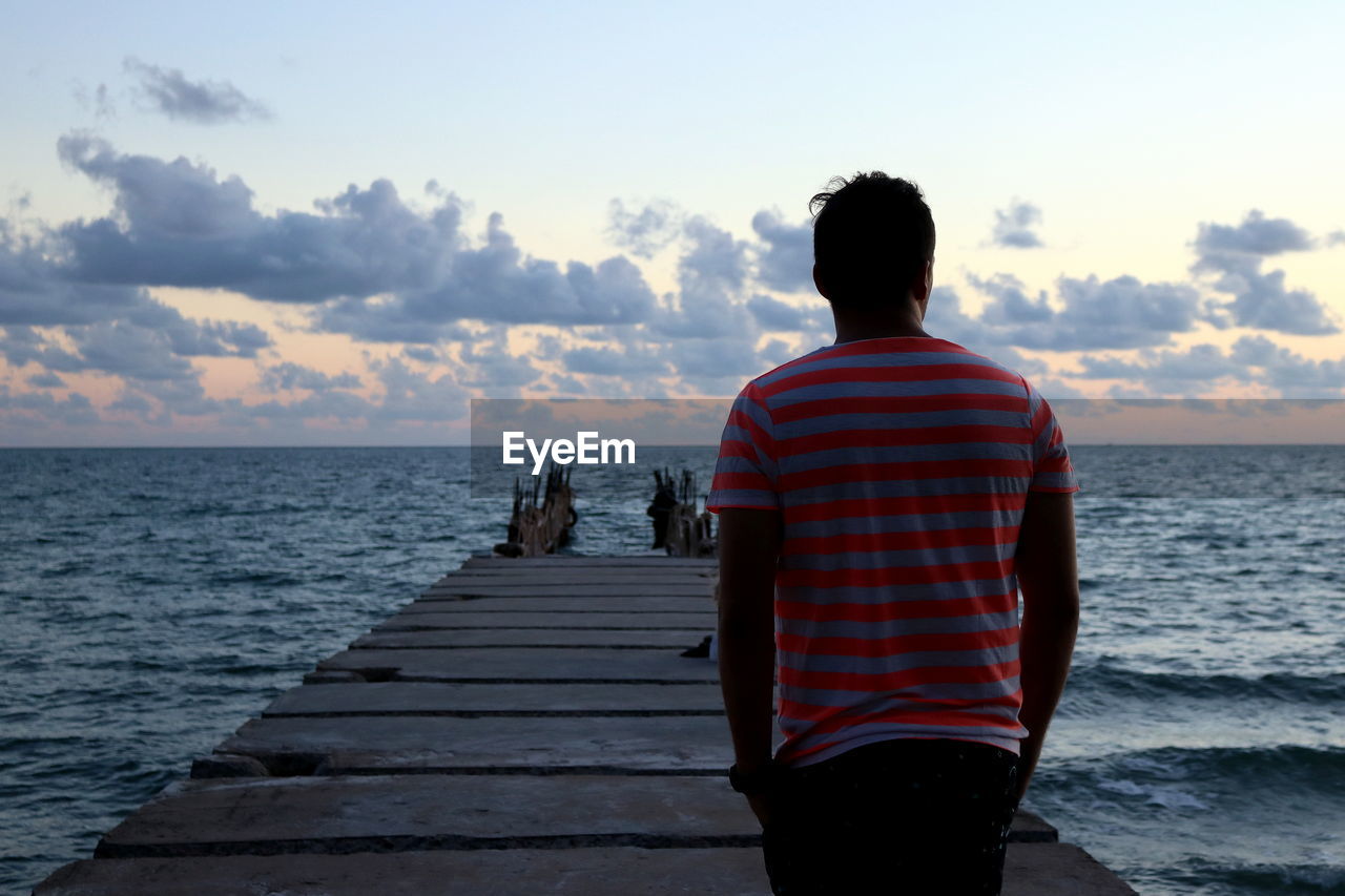 Rear view of man standing on pier over sea against sky