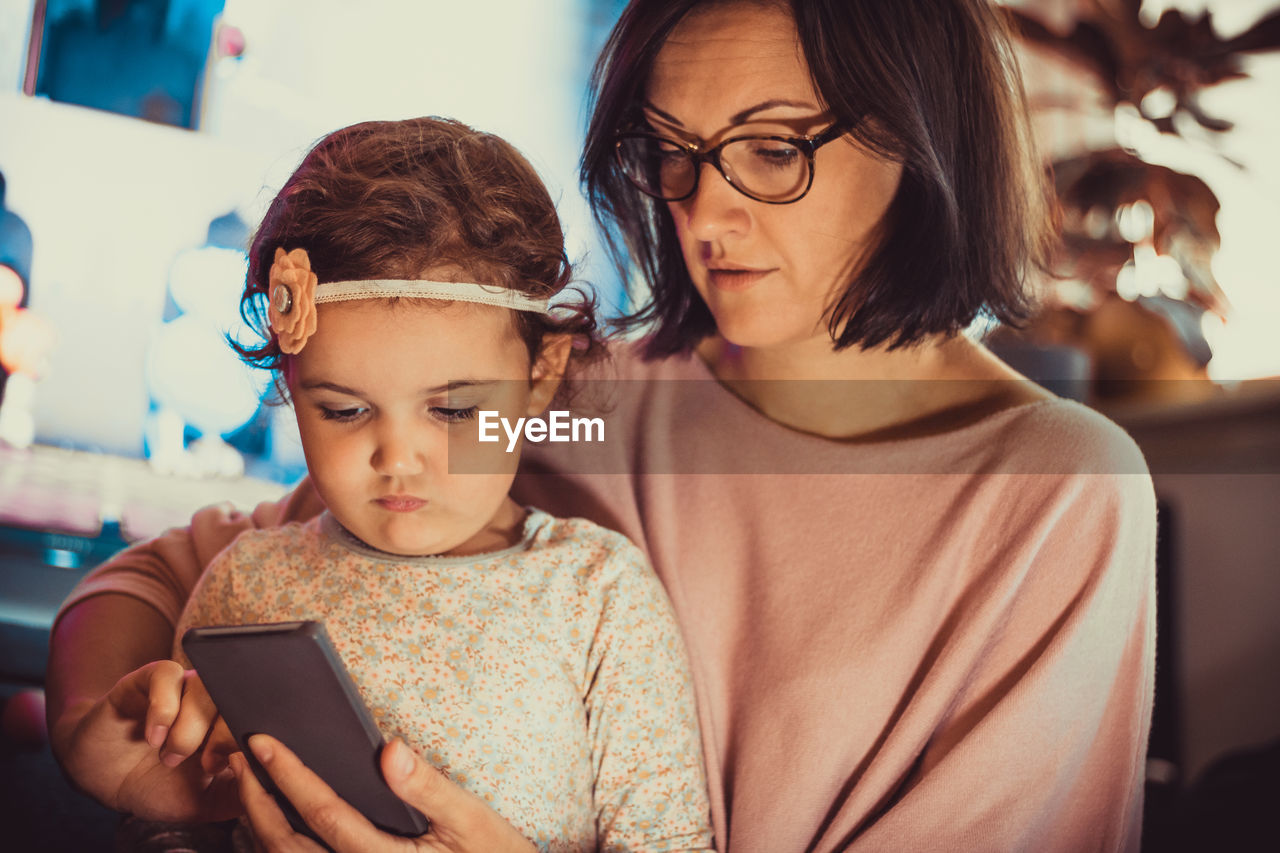 Mother and daughter using mobile phone while spending time together at home.